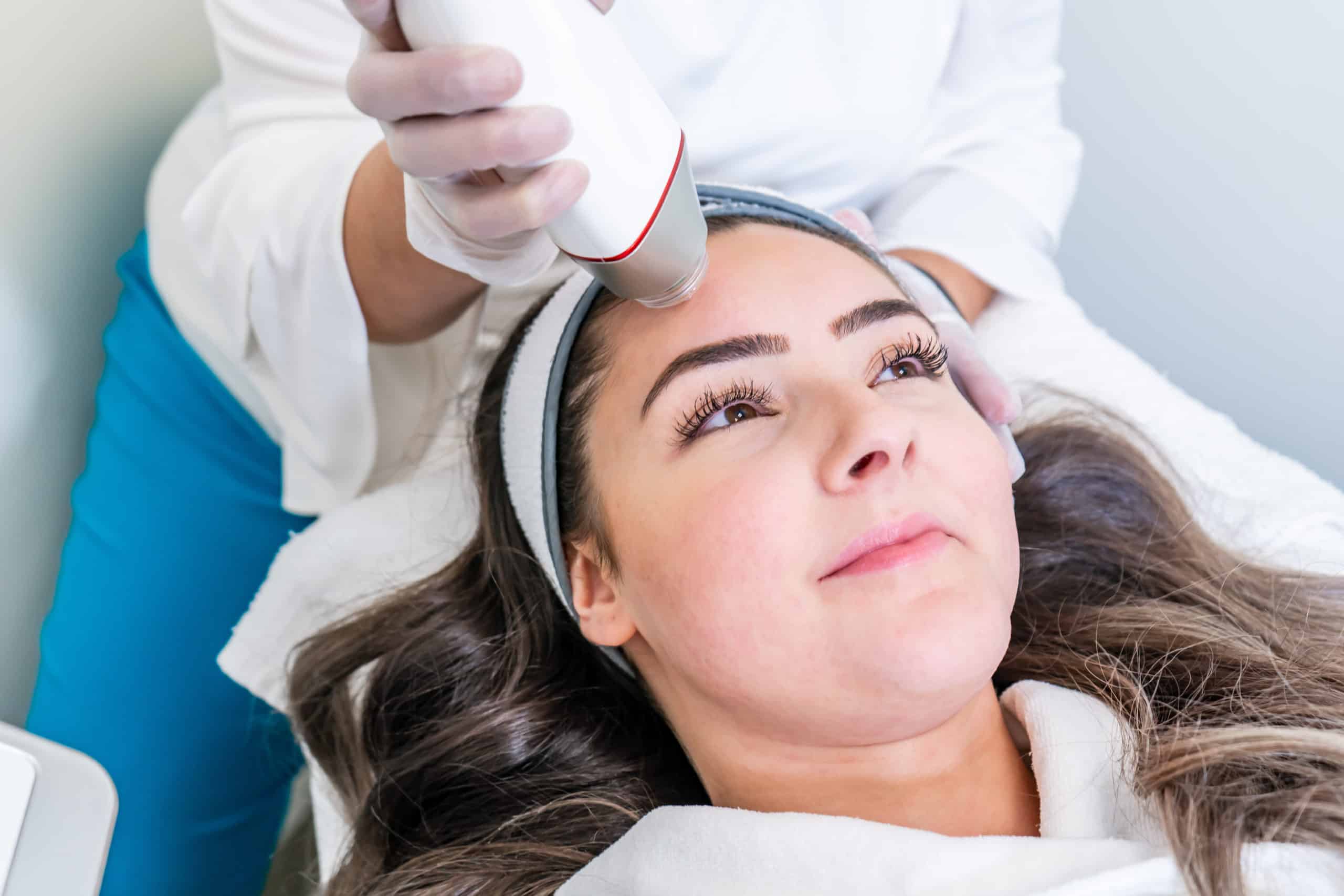 Beauty treatment using microneedling device with radio frequency to tighten skin. Used on the forehead of a woman during treatment.